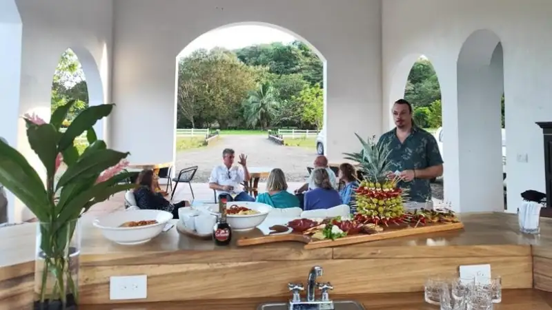 Tropical open-air dining area with a buffet setup, guests, and lush surroundings.