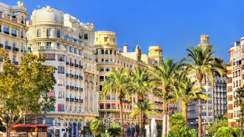 Historic buildings and palm trees in Plaza del Ayuntamiento, Valencia, Spain, on a sunny day.