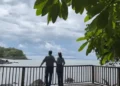 Lief and Kathleen standing together on a wooden viewing deck, gazing out over a calm ocean surrounded by lush greenery and a cloudy sky.