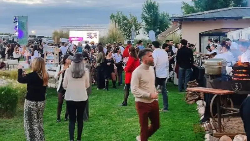 People gathered at an outdoor food and wine event with chefs cooking and guests socializing on a grassy area.