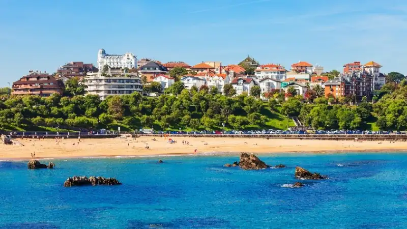 Coastal view of Santander, Spain with sandy beach, turquoise water, and hillside homes.