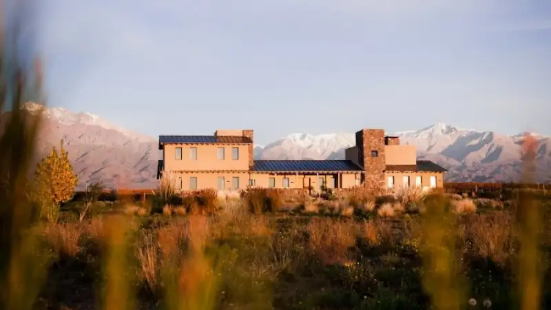 House in a grassy field with snow-capped mountains in the background at sunset.