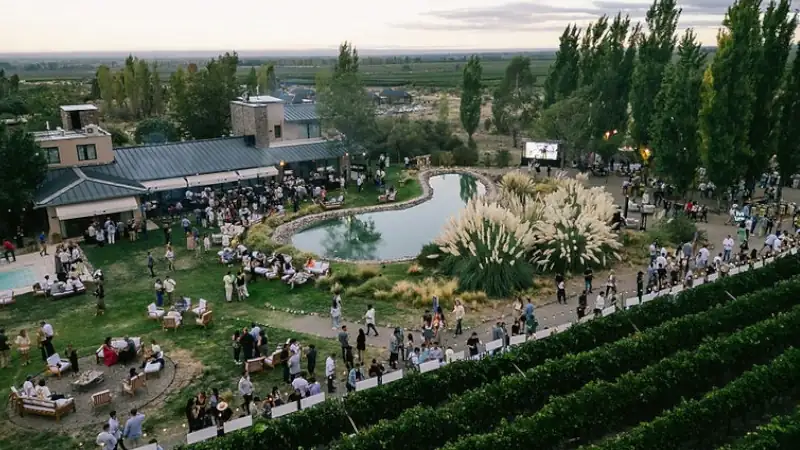 Outdoor event at a vineyard with crowds around a pond and seating areas.