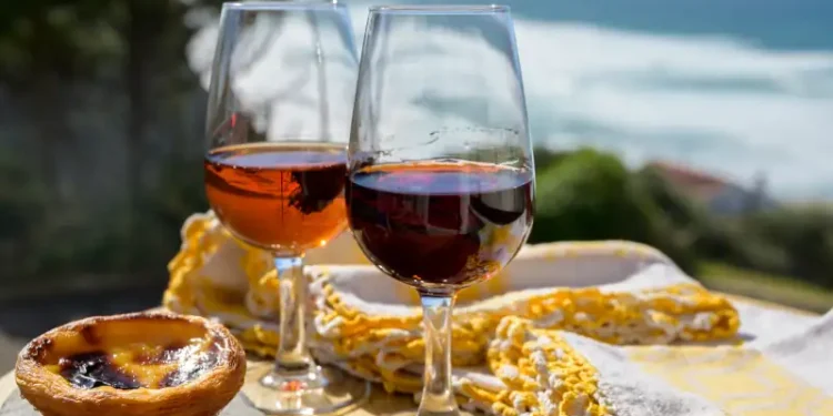Portugal's traditional food and drink, glass of porto wine, muscatel and sweet dessert Pastel de nata egg custard tart pastry served with view on blue Atlantic ocean in Lisbon area, Portugal
