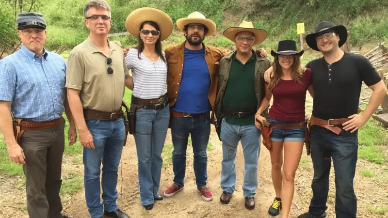 Lief, Kathleen, and five others in Western-style clothing and cowboy hats pose together at an outdoor shooting range.