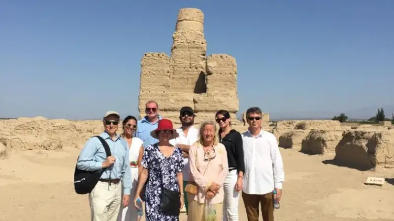 A group of nine people pose for a photo in front of ancient desert ruins under a clear blue sky.