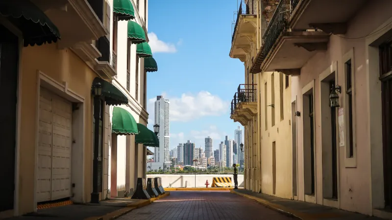 A colorful alley on a sunny day in the old town Casco Viejo with the skyline of Panama City in the background.