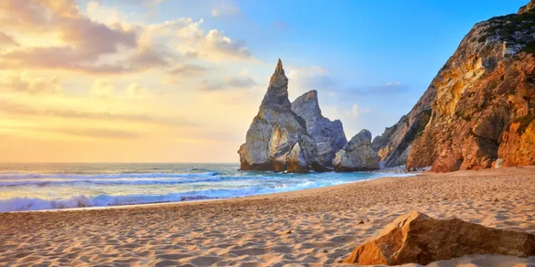 Portugal Ursa Beach at atlantic coast of Atlantic Ocean with rocks and sunset sun waves and foam at sand of coastline picturesque landscape panorama.