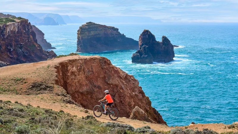 happy active senior woman cycling on the the rocky cliffs of the Vicentina coast of Algarve, Portugal near Sagres and Vila do Bispo