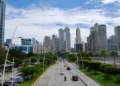 Panama City’s Avenida Balboa with cars on a coastal highway, lined with green parks and modern high-rise buildings under a partly cloudy sky.