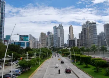 Panama City’s Avenida Balboa with cars on a coastal highway, lined with green parks and modern high-rise buildings under a partly cloudy sky.