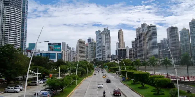 Panama City’s Avenida Balboa with cars on a coastal highway, lined with green parks and modern high-rise buildings under a partly cloudy sky.