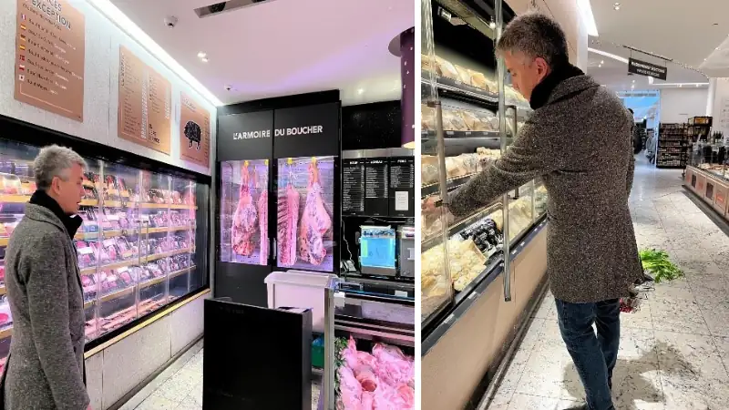 Lief Simon browsing meat displays inside a butcher shop or grocery store, looking at refrigerated cases of cuts and poultry.