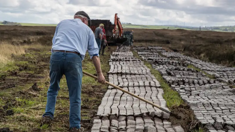 Men cutting turf in a peat bog field in rural Ireland
