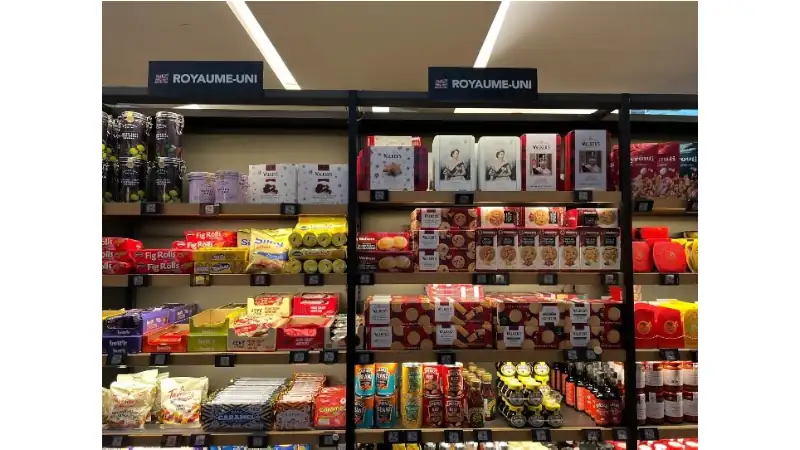 Shelves in a grocery store displaying a variety of British food products, including biscuits, snacks, and preserves, under signs labeled ‘Royaume-Uni.