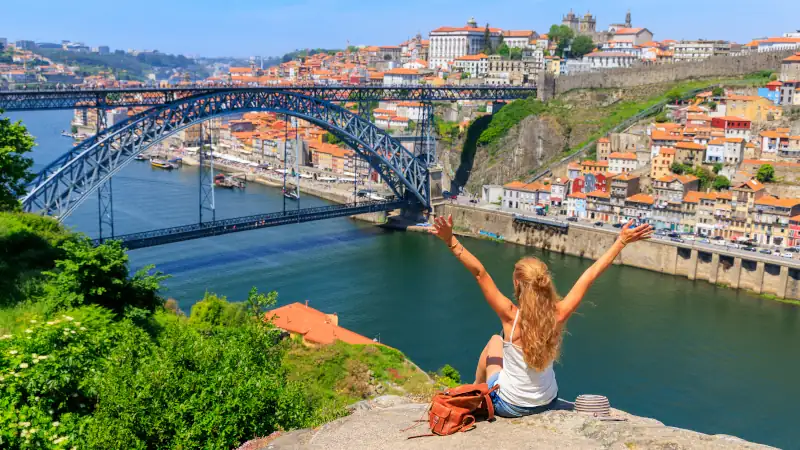 Woman touristwith arms raised enjoying beautiful panoramic view of famous iron bridge and old town- tour tourism in Portugal, travel in Porto
