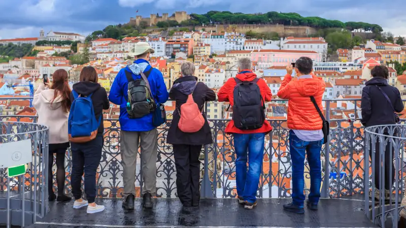 Group of tourists watching the cityscape of Lisbon and taking pictures to Sao Jorge castle in Portugal