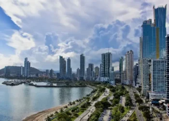 Panama City’s waterfront skyline with tall modern towers, a curving coastal highway, and the bay in the foreground on a bright, partly cloudy day.