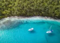 San Blas Islands, Panama - Aerial Drone Top Down View of two Sailing Yachts anchored in Turquoise Water right next to perfect White Sand Beach of Caribbean Tropical Island full of green Palm Trees.
