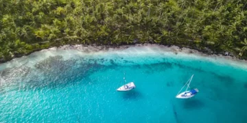 San Blas Islands, Panama - Aerial Drone Top Down View of two Sailing Yachts anchored in Turquoise Water right next to perfect White Sand Beach of Caribbean Tropical Island full of green Palm Trees.