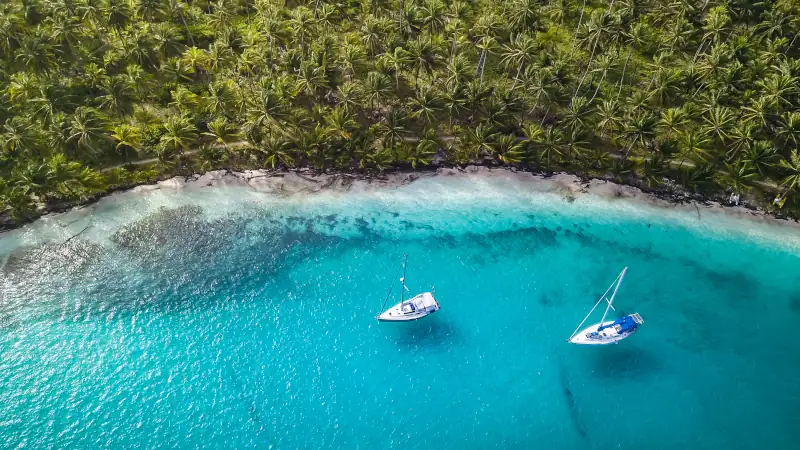 San Blas Islands, Panama - Aerial Drone Top Down View of two Sailing Yachts anchored in Turquoise Water right next to perfect White Sand Beach of Caribbean Tropical Island full of green Palm Trees.