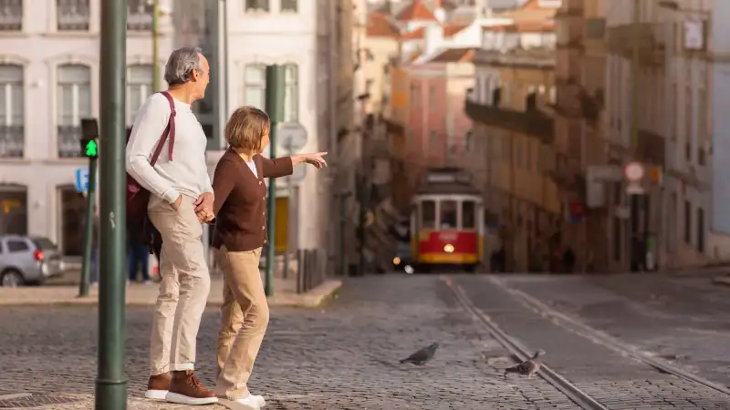 Senior Tourists Couple Walking In Lisbon, Pointing Finger At Tram