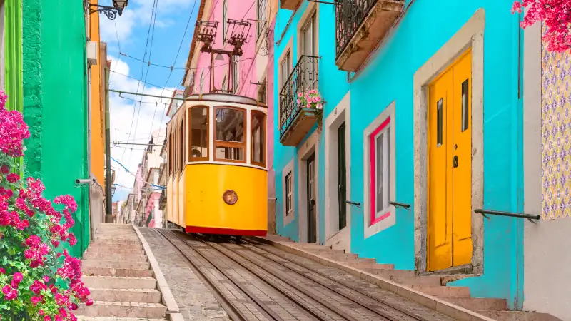 Lisbon, Portugal - Yellow tram on a street with colorful houses and flowers on the balconies - Bica Elevator going down the hill of Chiado.