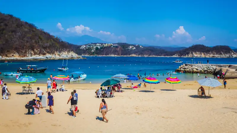 People walking on a white sandy beach in Huatulco during summer.