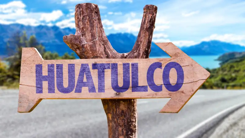 Wooden sign pointing to Huatulco, Mexico on a road background.
