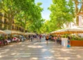 Tourists walk past sidewalk cafes on the famous La Rambla street through the historic Mediterranean city of Barcelona, Catalonia, Spain.