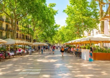 Tourists walk past sidewalk cafes on the famous La Rambla street through the historic Mediterranean city of Barcelona, Catalonia, Spain.