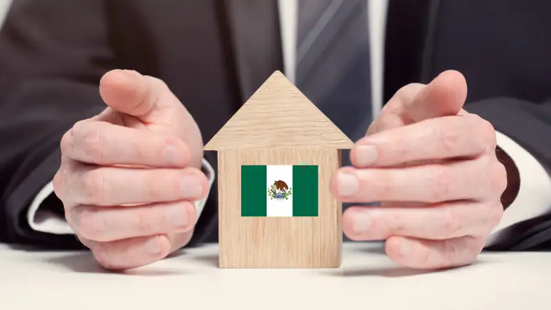 Businessman hand holding wooden home model with Mexican flag.