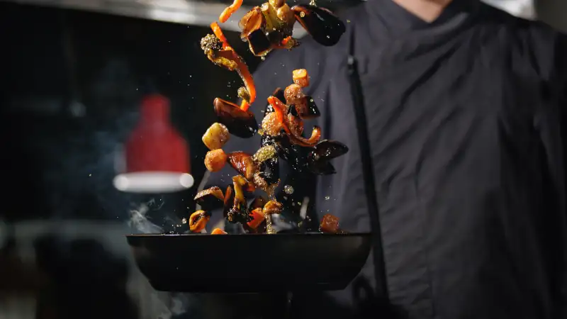 Chef tossing vegetables in a pan, symbolizing skilled labor and culinary work