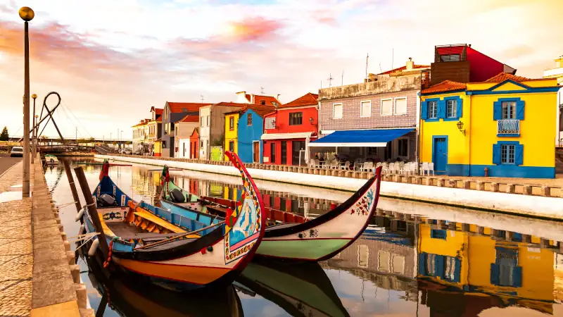 Traditional colorful Moliceiro boats docked in the water canal among historical buildings.