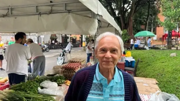 An elderly man smiles at the camera under a market tent