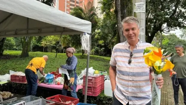 Lief Simon smiling and holding yellow flowers stands near an outdoor market stall