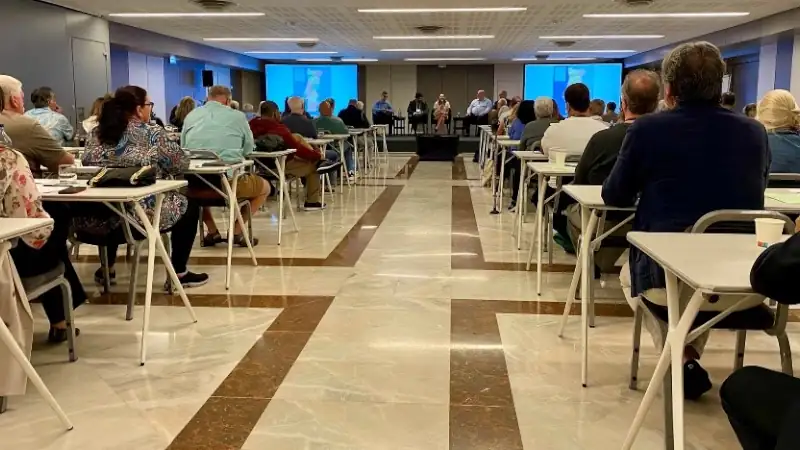 Attendees seated in a conference hall listening to a panel discussion with speakers presenting at the front of the room.