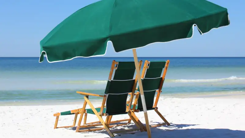 Two chairs and green umbrella on white sand beach