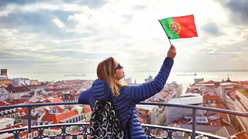 Young woman tourist enjoying beautiful cityscape top view on the old town holding the flag of Portugal in hands during the sunny day in Lisbon city