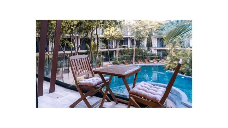A charming poolside patio in Tulum, featuring a wooden table and cushioned chairs overlooking a crystal-clear pool