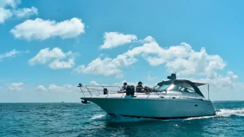 A sleek white yacht cruising across calm blue ocean waters under a bright sky with scattered clouds.