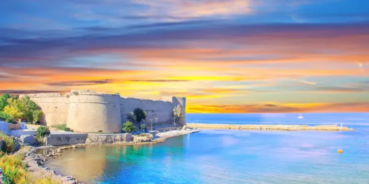 Historic seaside fortress in North Cyprus overlooking calm turquoise waters at sunset, with soft golden and pastel skies reflecting across the coastline.