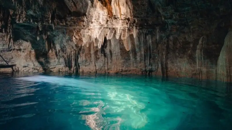 Crystal-clear turquoise water inside a natural cave with textured rock walls and soft light reflecting on the surface.