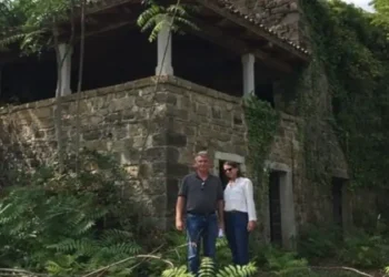 Lief and Kathleen standing outside a rustic stone home surrounded by lush greenery during their renovation project.