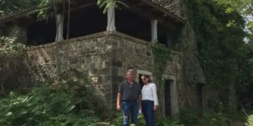 Lief and Kathleen standing outside a rustic stone home surrounded by lush greenery during their renovation project.
