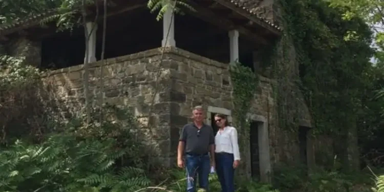 Lief and Kathleen standing outside a rustic stone home surrounded by lush greenery during their renovation project.