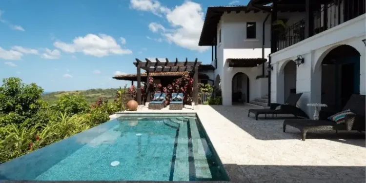 Luxury villa at Los Islotes featuring an infinity pool, covered terrace, and tropical hillside views under a bright blue sky.