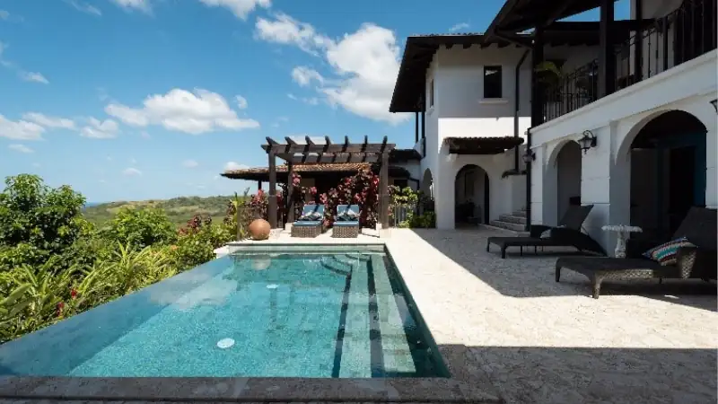 Luxury villa at Los Islotes featuring an infinity pool, covered terrace, and tropical hillside views under a bright blue sky.