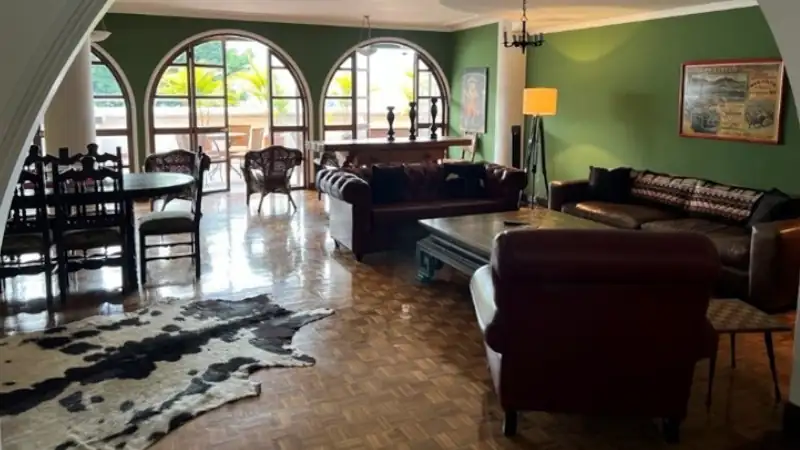 Elegant Medellín apartment living room with arched windows, green accent walls, leather furniture, and polished parquet floors.