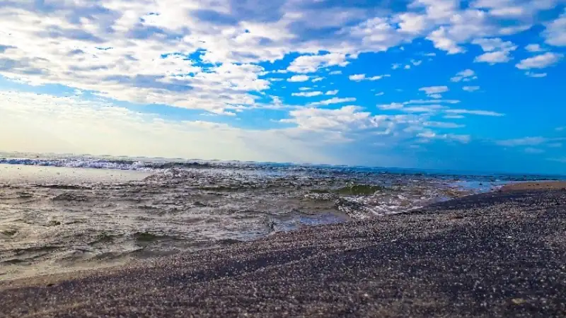 Rugged Panamanian shoreline with dark volcanic-looking pebbles, gentle ocean waves, and a dramatic tropical sky.